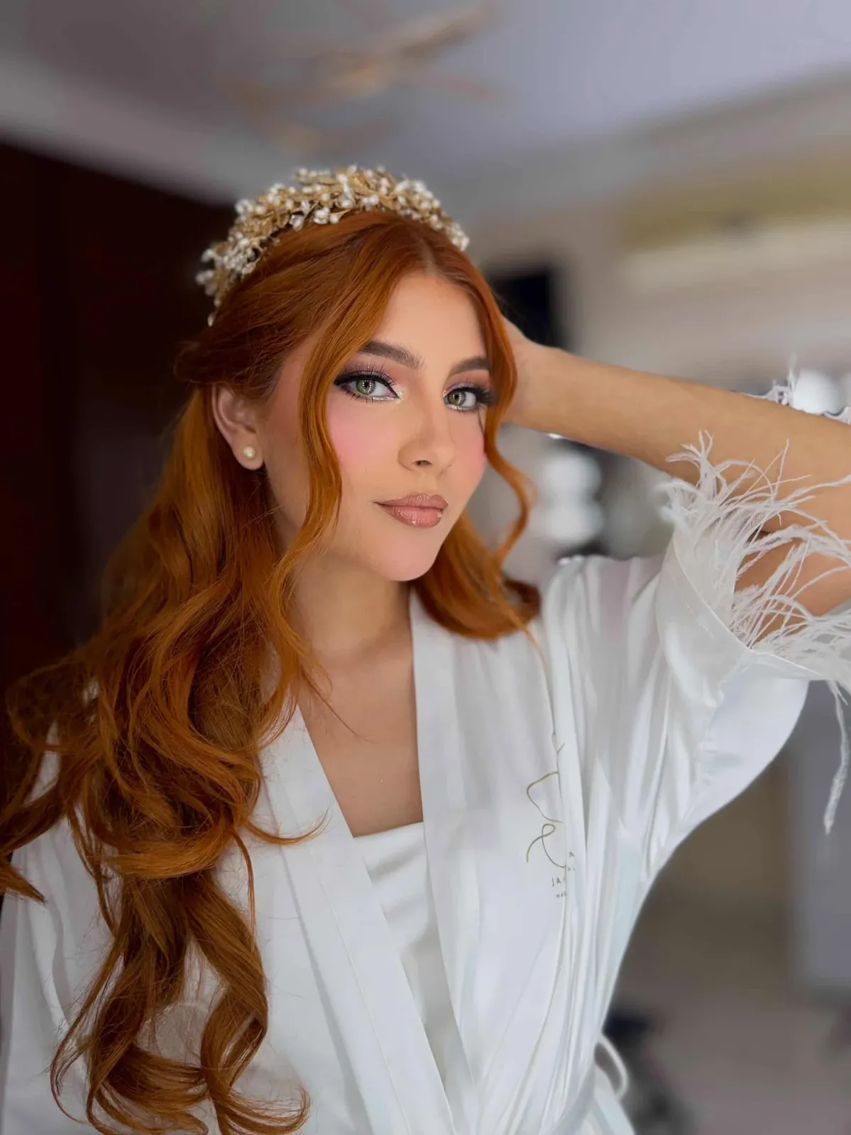 Novia pelirroja con corona dorada de perlas y maquillaje glam durazno